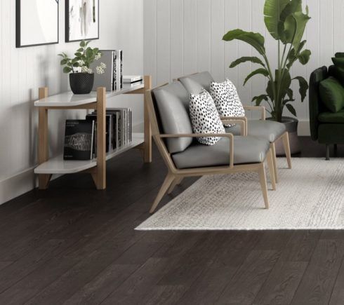 Living room with dark wood floors, gray chairs, white rug, and wood shelf.