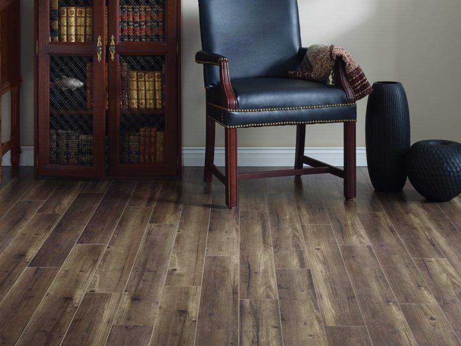 Wooden floor with a bookcase, leather chair, and black vases against a beige wall.