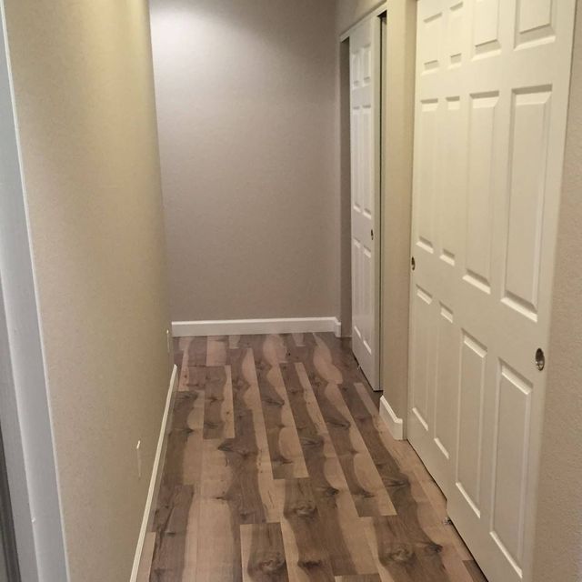 Narrow hallway with wood-look flooring and white doors on one side. Beige walls.