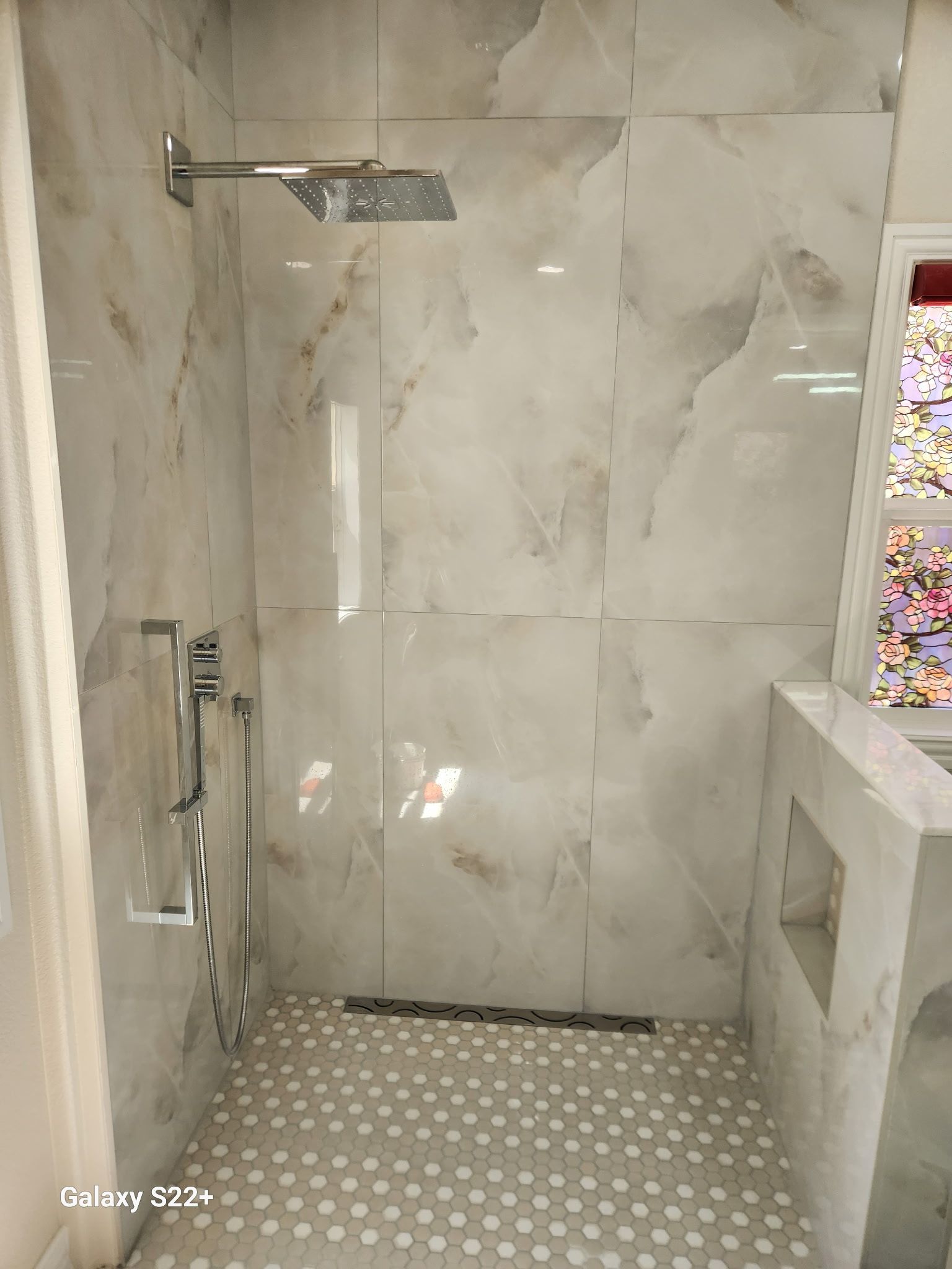 Modern tiled bathroom shower with glass door, wall-mounted showerhead, and mosaic tile floor