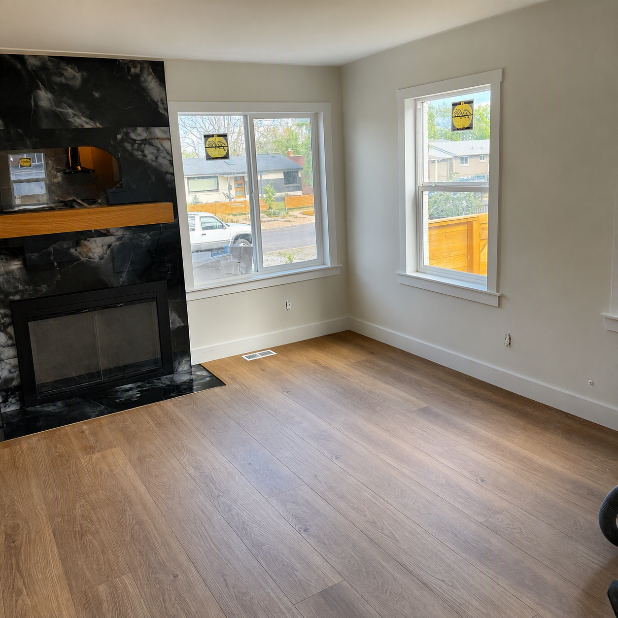 Empty living room with wood floors, white walls, two windows, and a black stone fireplace.
