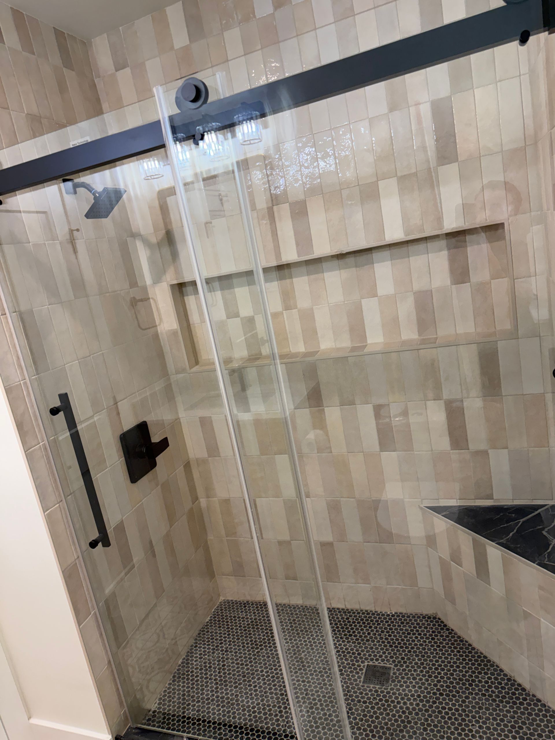 Glass shower enclosure with tiled walls, pebble floor, and a built-in shelf in a bathroom