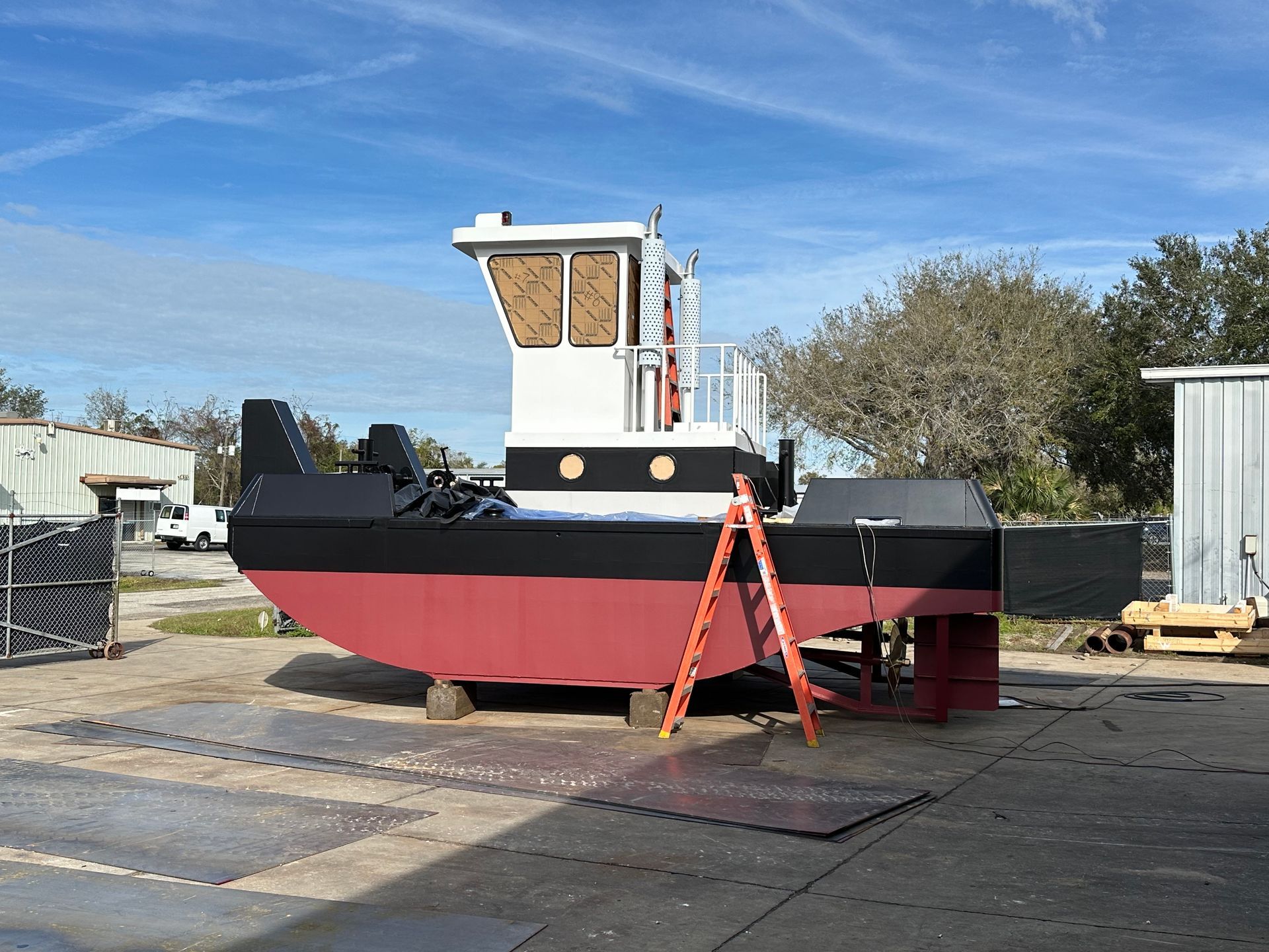 A red and black boat with a ladder attached to it is parked in a parking lot.
