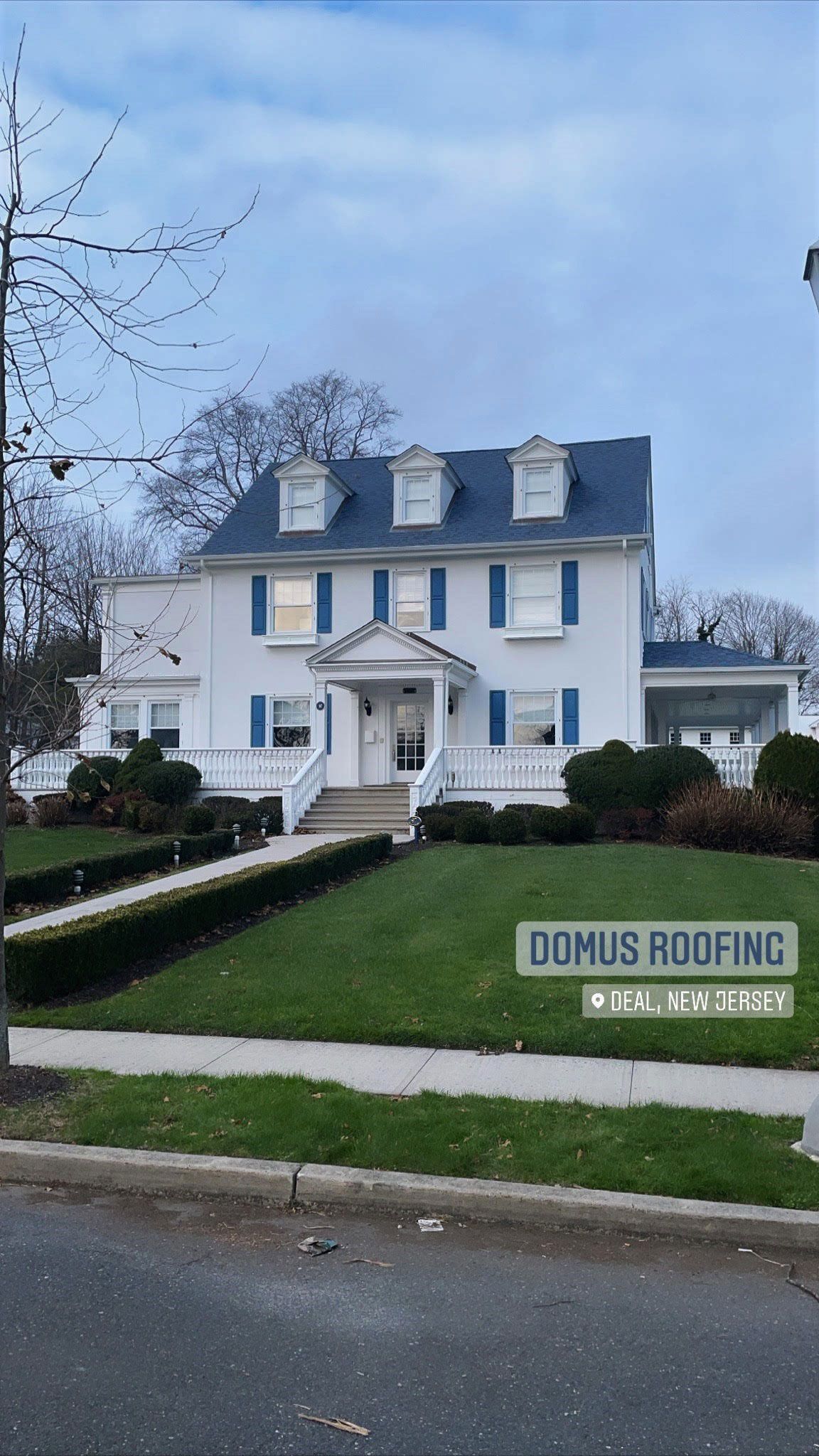 A large white house with a blue roof is sitting on top of a lush green lawn.