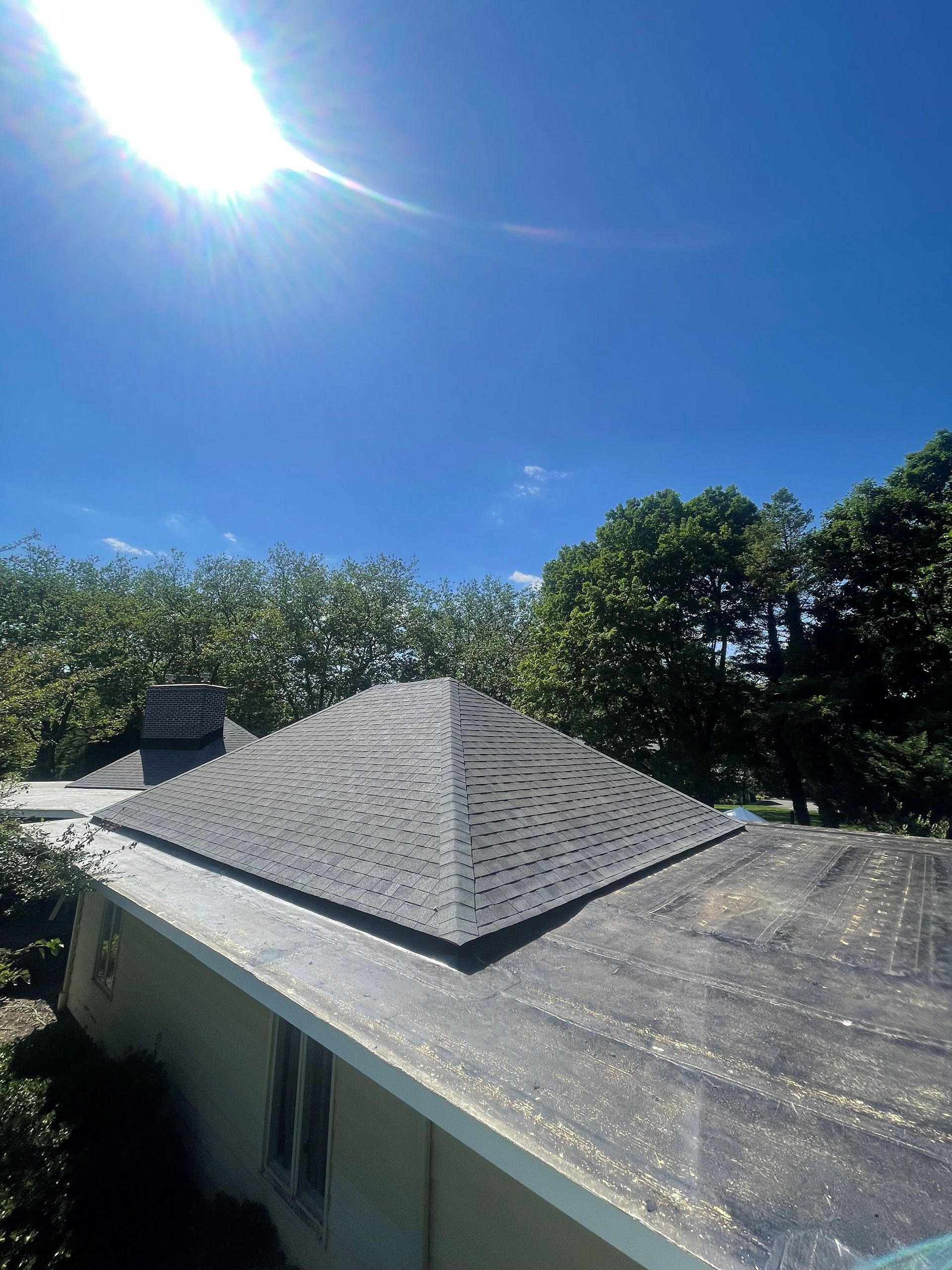 The sun is shining brightly on the roof of a house surrounded by trees