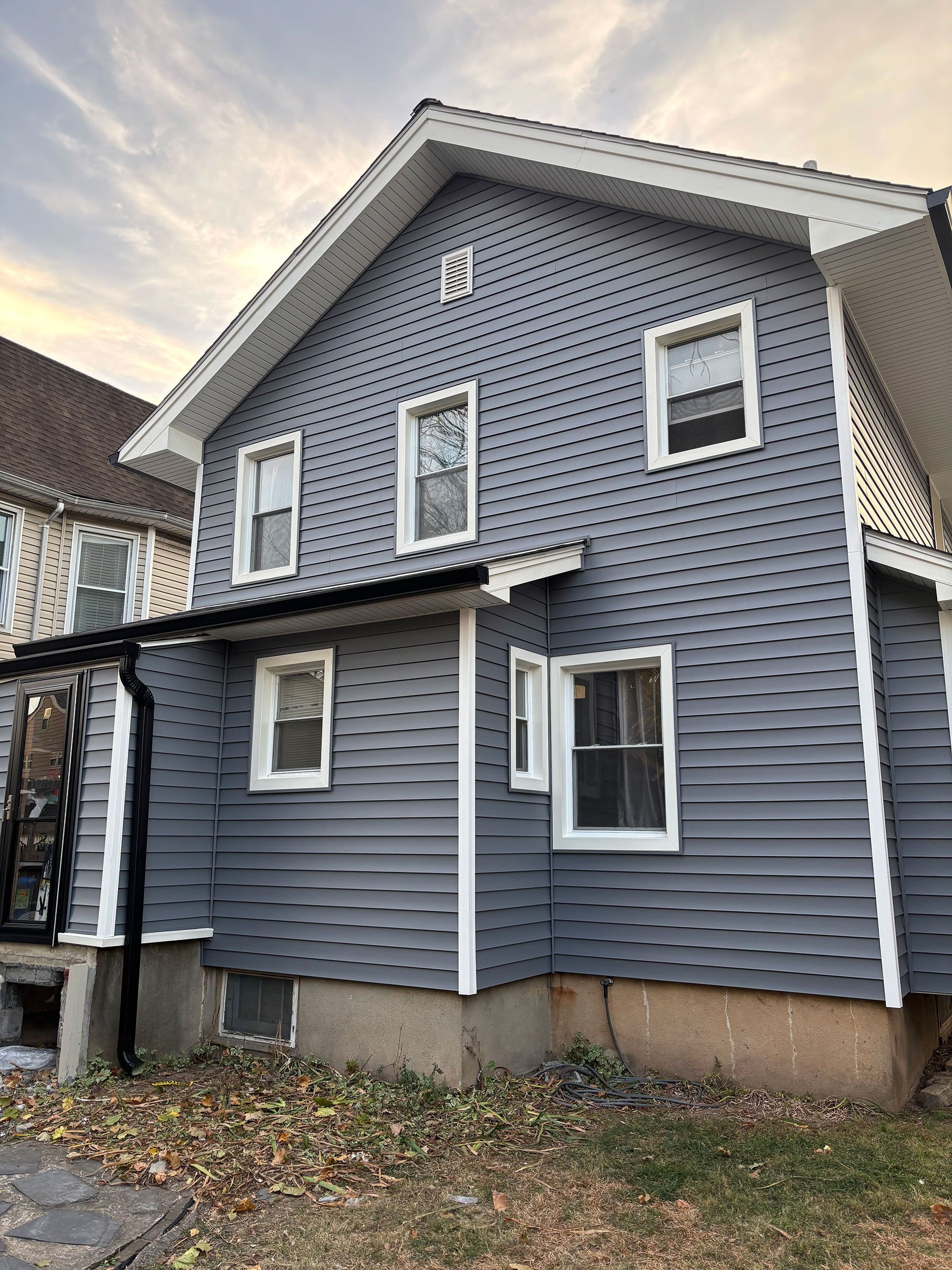A gray house with white trim and windows is sitting on top of a lush green field
