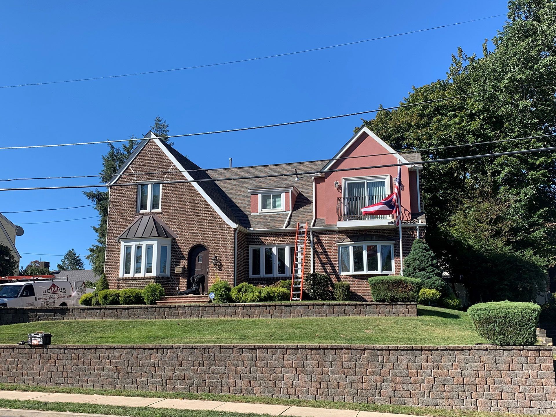 A large brick house with a red roof is sitting next to a brick wall