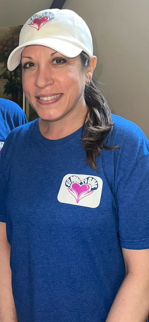 Two people wearing matching blue shirts and white hats with a logo, smiling indoors.