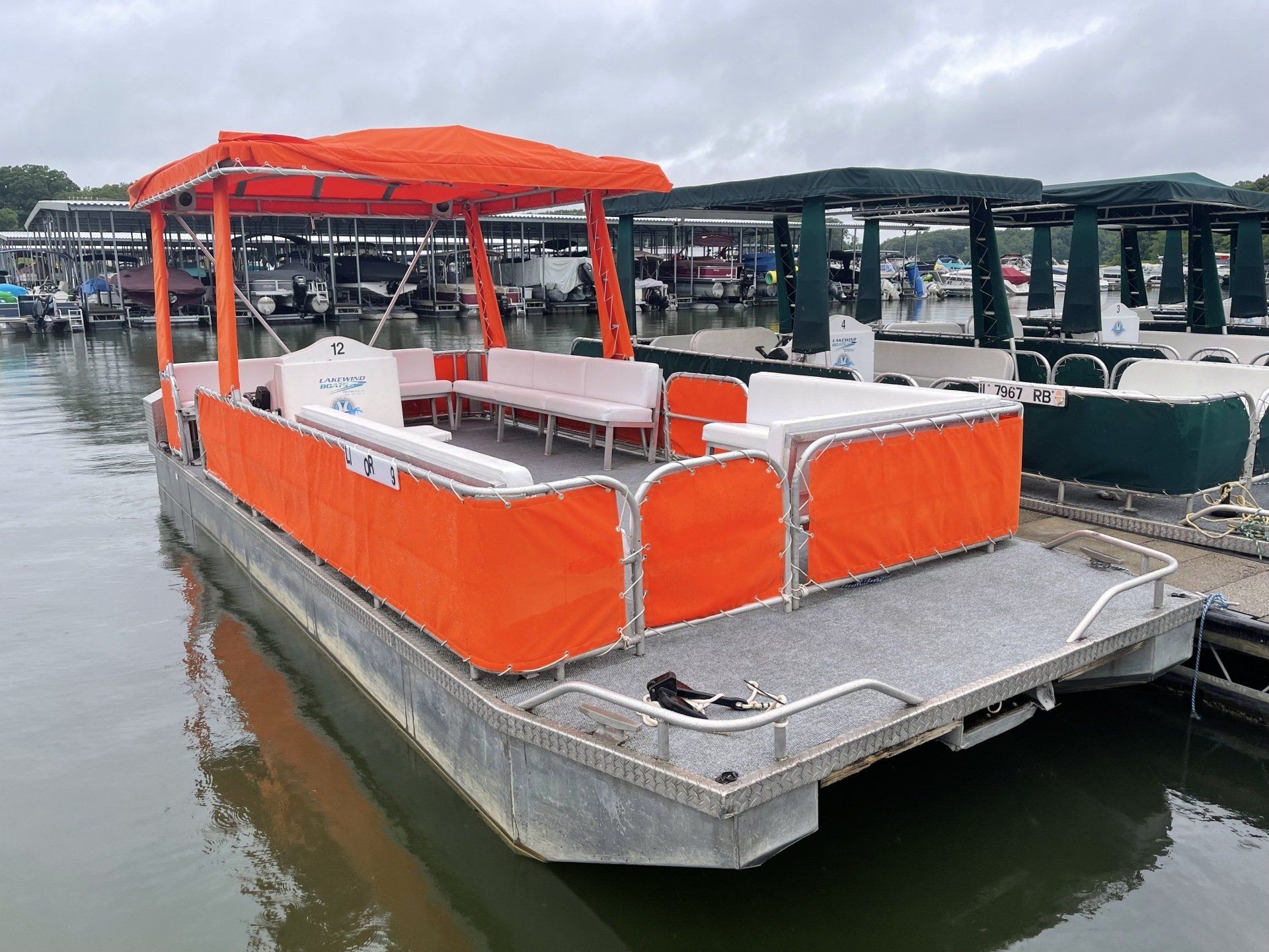 Orange pontoon boat docked at a marina with white seating under a matching canopy.