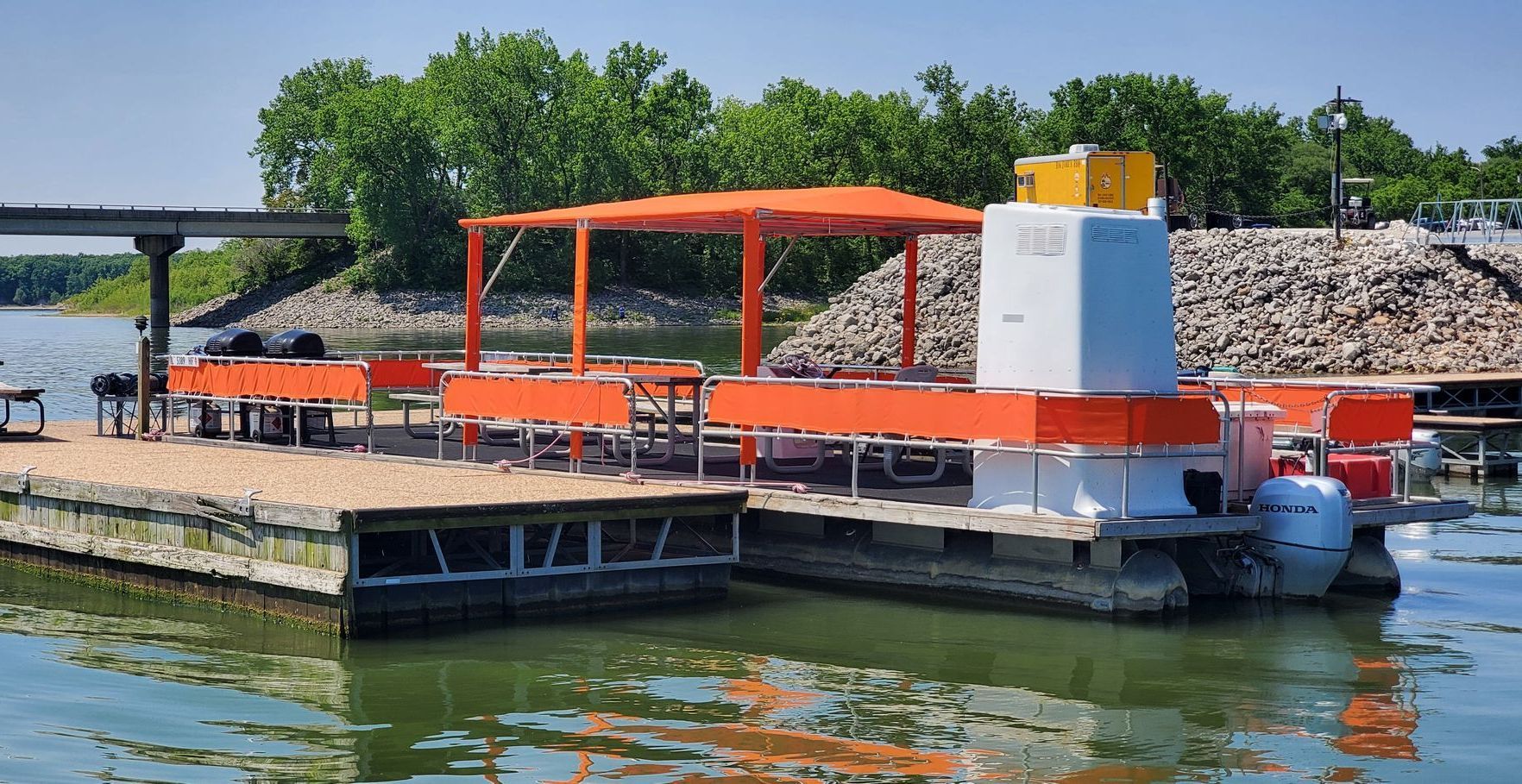 Floating orange dock with a pergola, grill, and white structure on a lake.