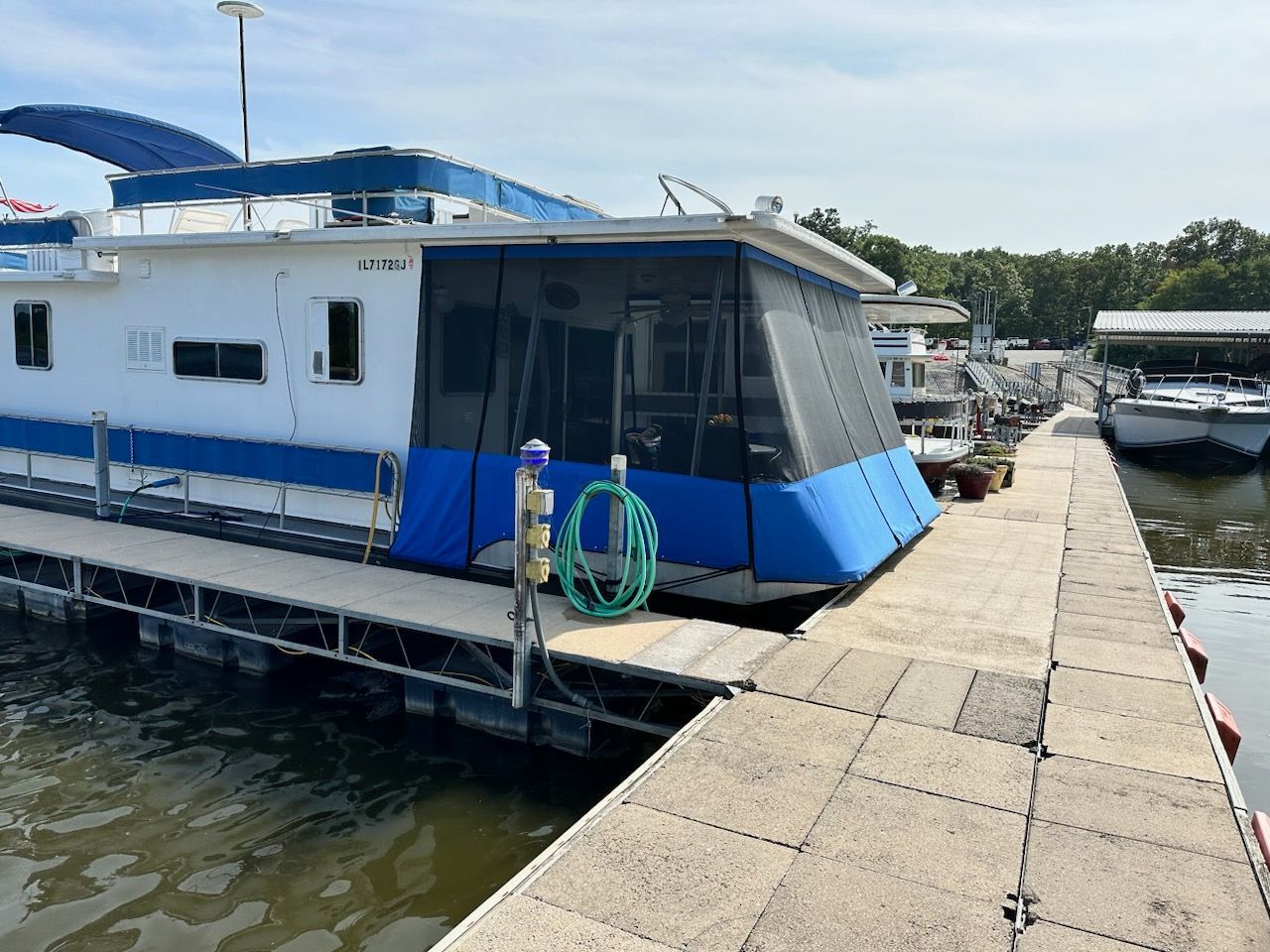 Houseboat docked at a marina with blue accents and a screened-in porch.