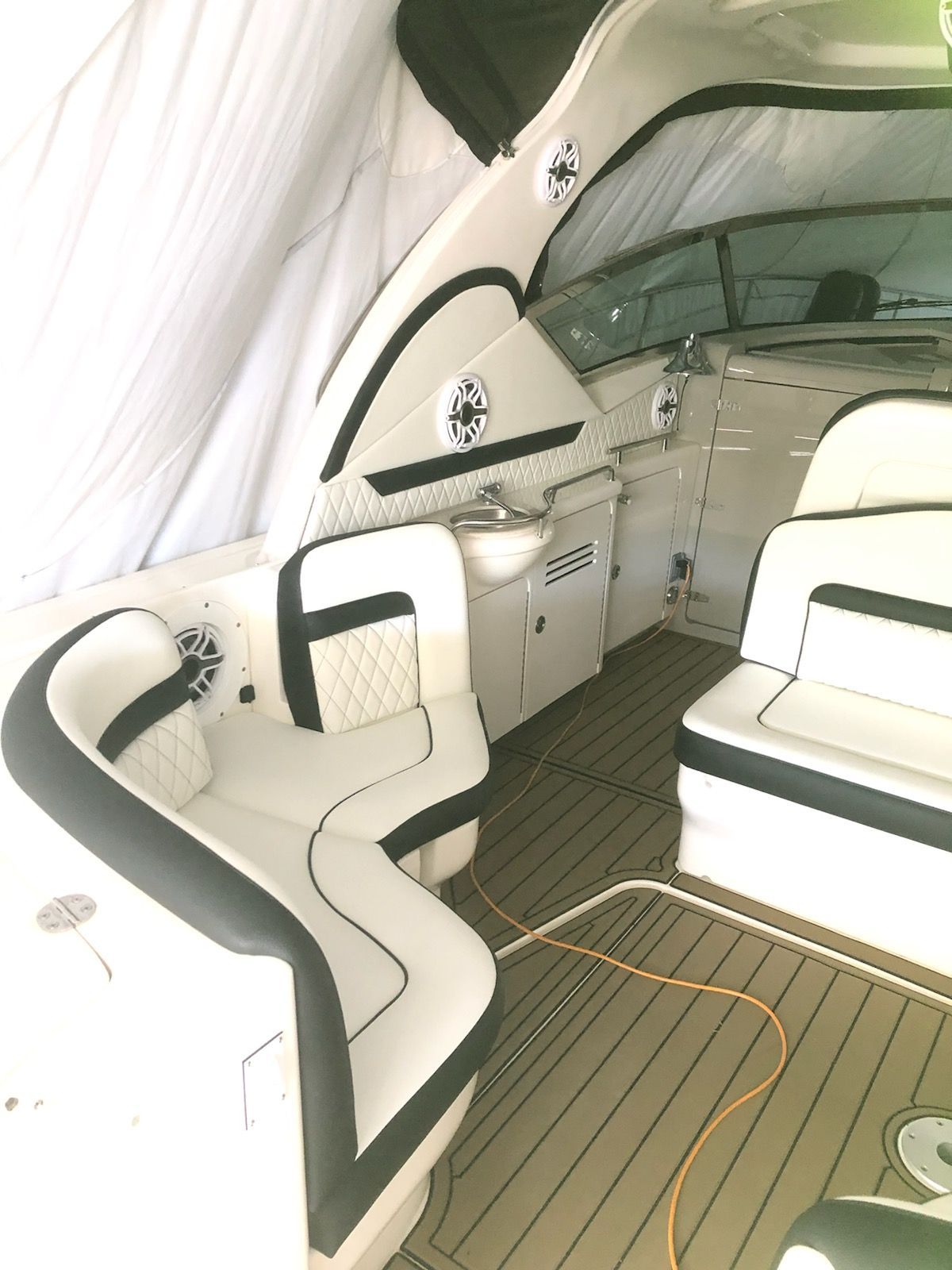 Boat interior with white and black seating, wooden flooring, and a small sink.