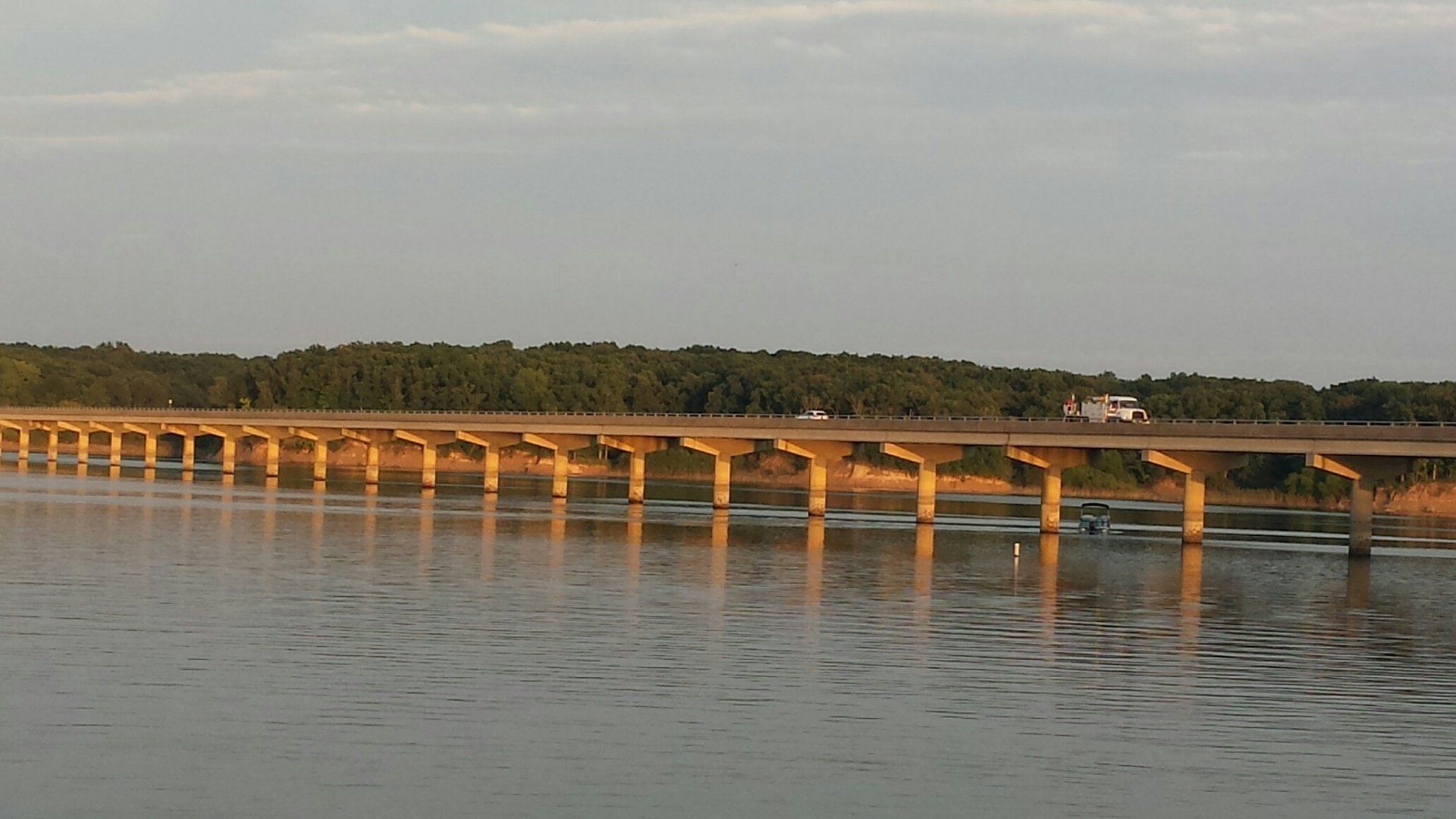 Long bridge over water with a few cars. Forest in the background.