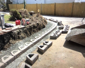 Construction of a retaining wall using concrete blocks along a gravel bed in a yard setting.