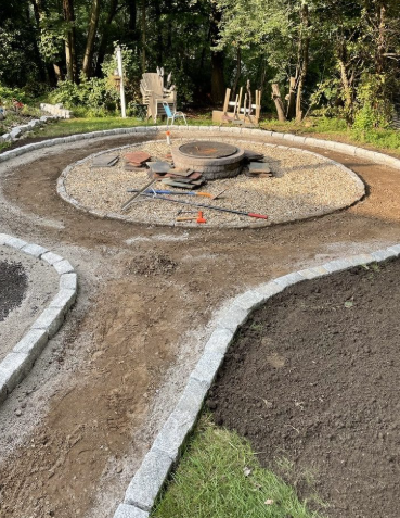 Garden with a circular fire pit and curved gravel paths bordered by stone edging.