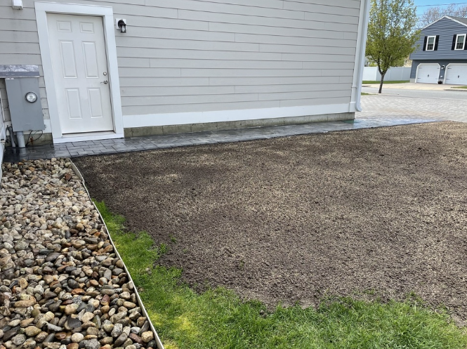 Yard with seeded area next to a building. Door on left, gravel border, and green grass.