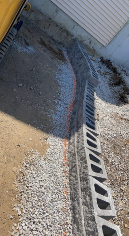A row of concrete blocks form a retaining wall, gravel and dirt fill the area near a building.