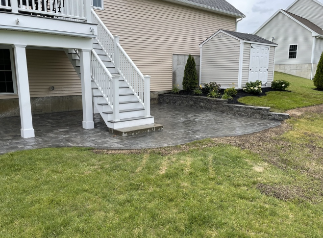 A backyard with a patio, stairs to a deck, small shed, and grassy lawn.