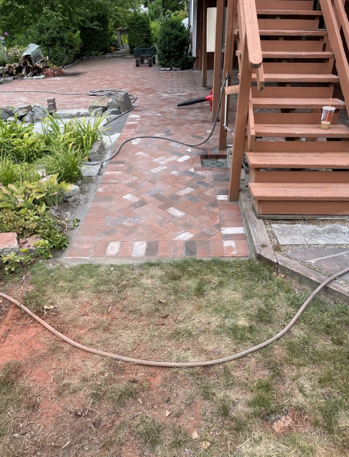 Brick pathway leading to wooden stairs, surrounded by grass and plants.
