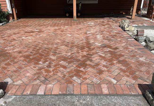 Red brick herringbone patio leading to a covered structure. Border of bricks at the edge.