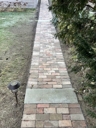 Brick pathway leading from view, flanked by grass and trees.