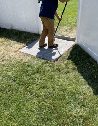 Person sweeping a small stone patio area between a white fence.