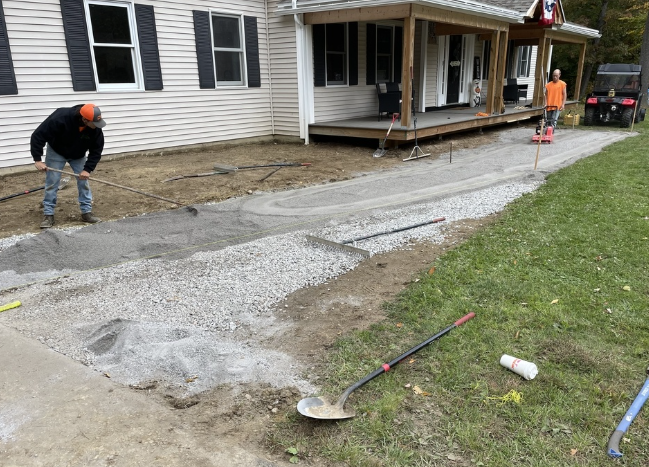 Workers laying gravel for a driveway near a house with a porch.