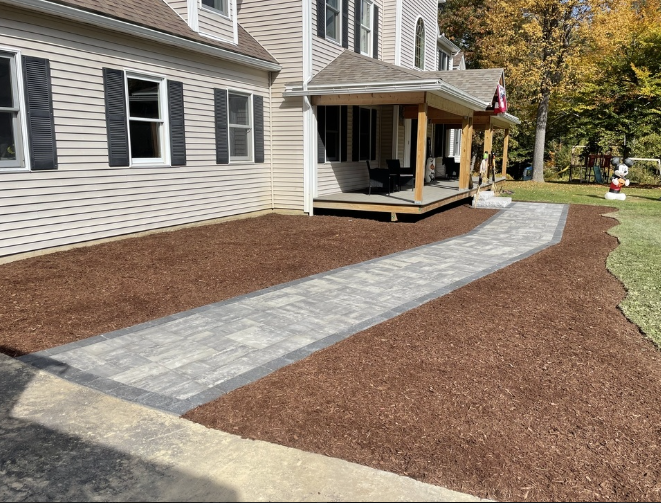 Paver walkway leading to a house porch with brown mulch beds on either side.