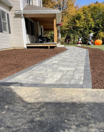 Stone paver walkway leading to a house with a porch, lined by dark mulch.