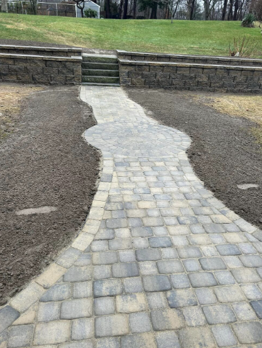 Stone walkway curves up to steps built into a retaining wall, on a grassy hillside.