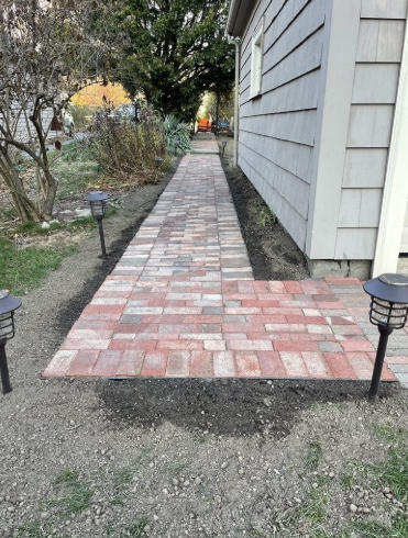 Brick walkway with solar lights next to a house.