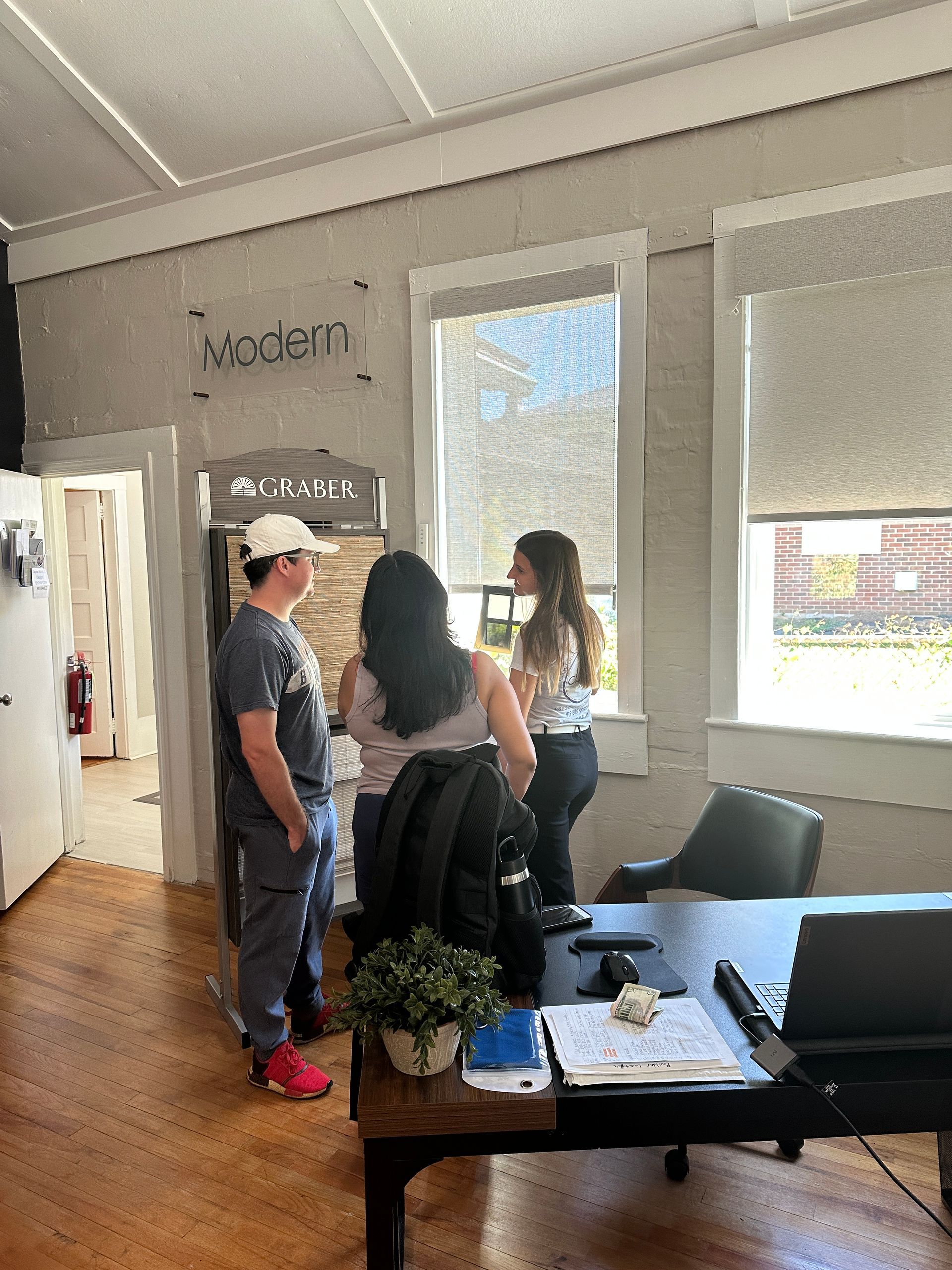 Three people in an office. One near a window, two near a doorway. 