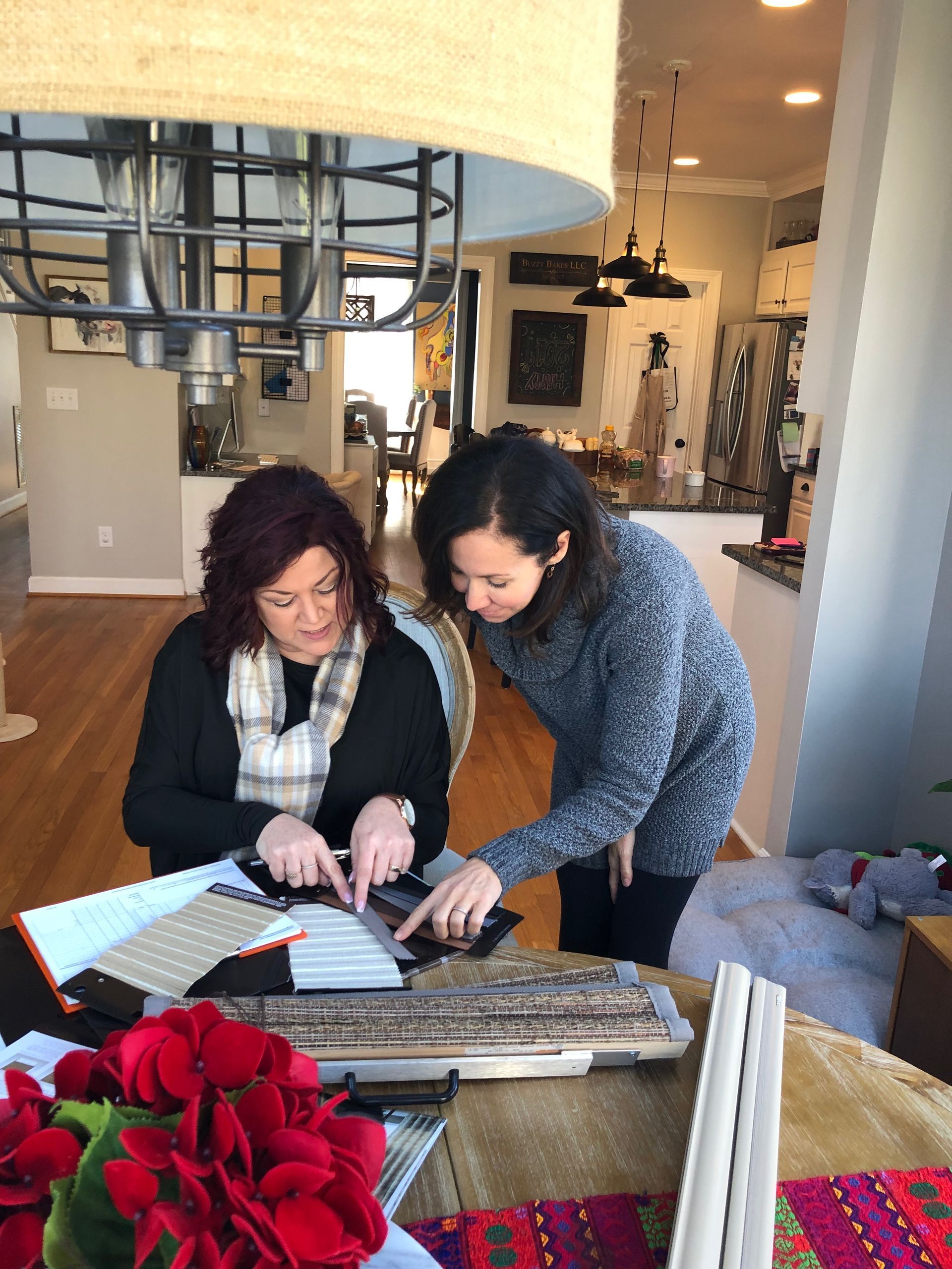 Two women looking at design samples on a table; interior setting with a kitchen in the background.