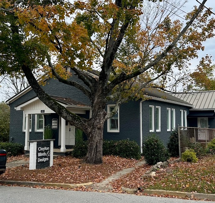 Dark blue building with white trim, Clayton Mink & Designs sign, large tree, fall leaves.