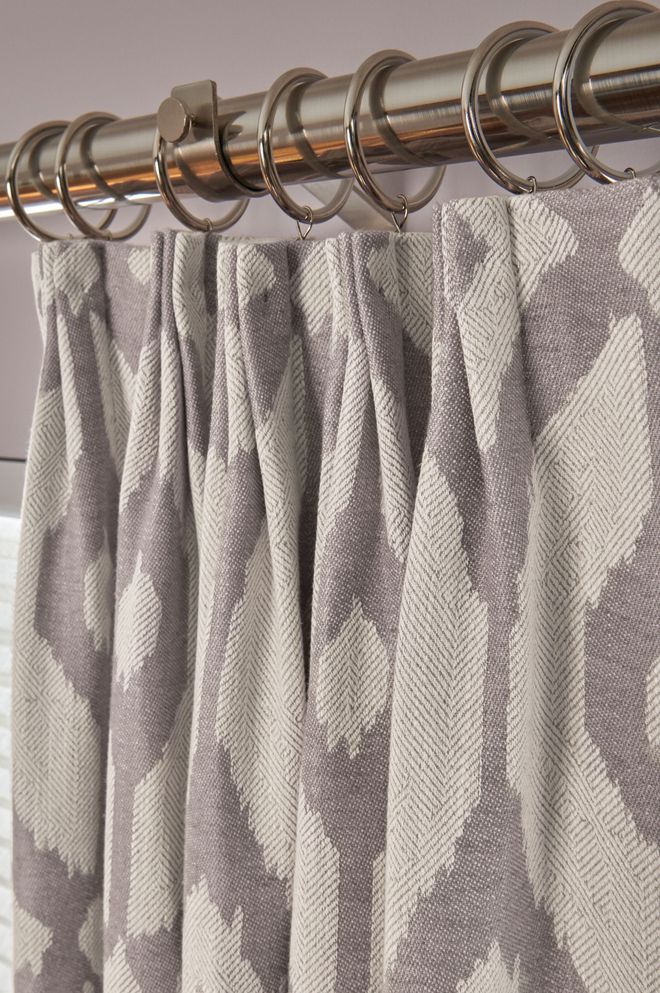 Gray and white patterned curtains with pleats hanging from a silver rod with rings.
