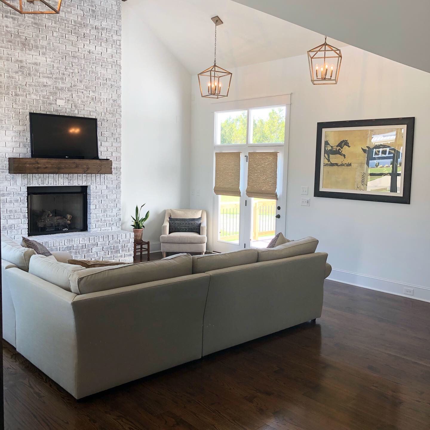 Living room with fireplace, white brick wall, and beige sofa. Dark wood floors, picture, and hanging lights.
