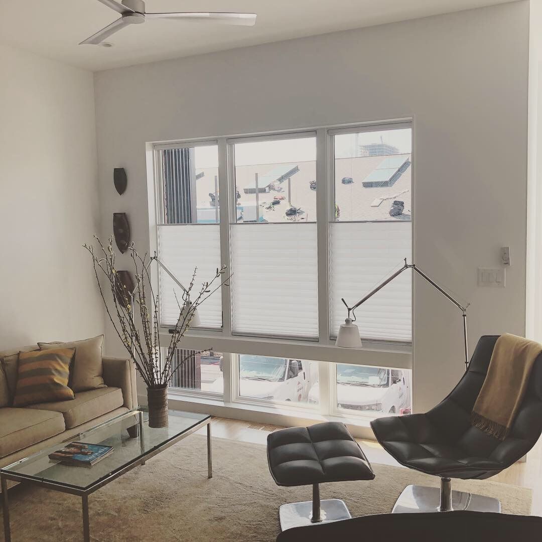 Living room with beige sofa, modern chair, large window with blinds.