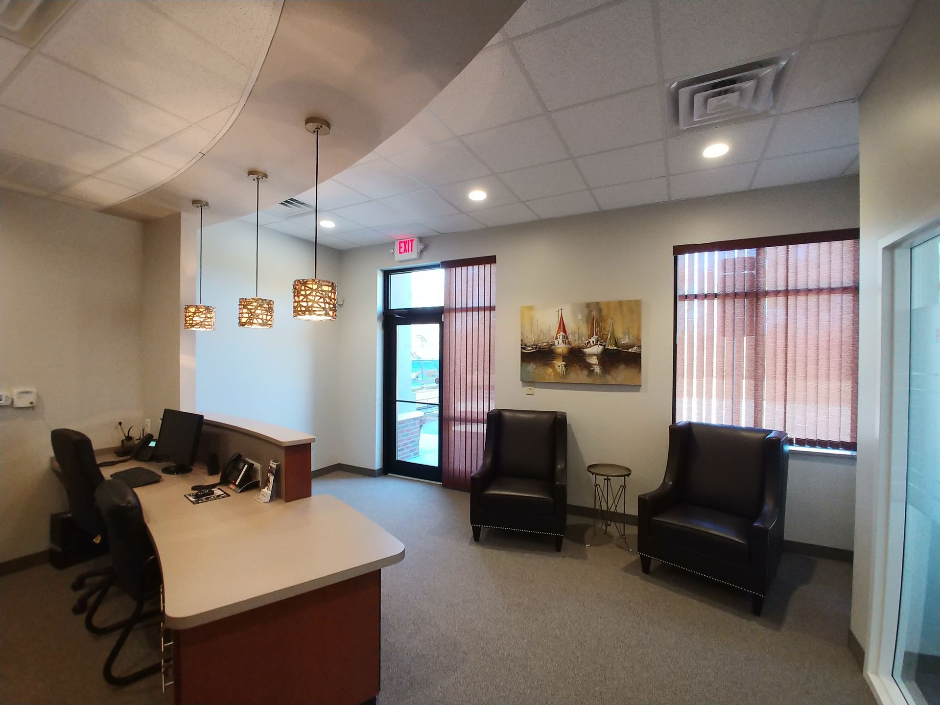 Reception area with desk, chairs, artwork, and door to outside.