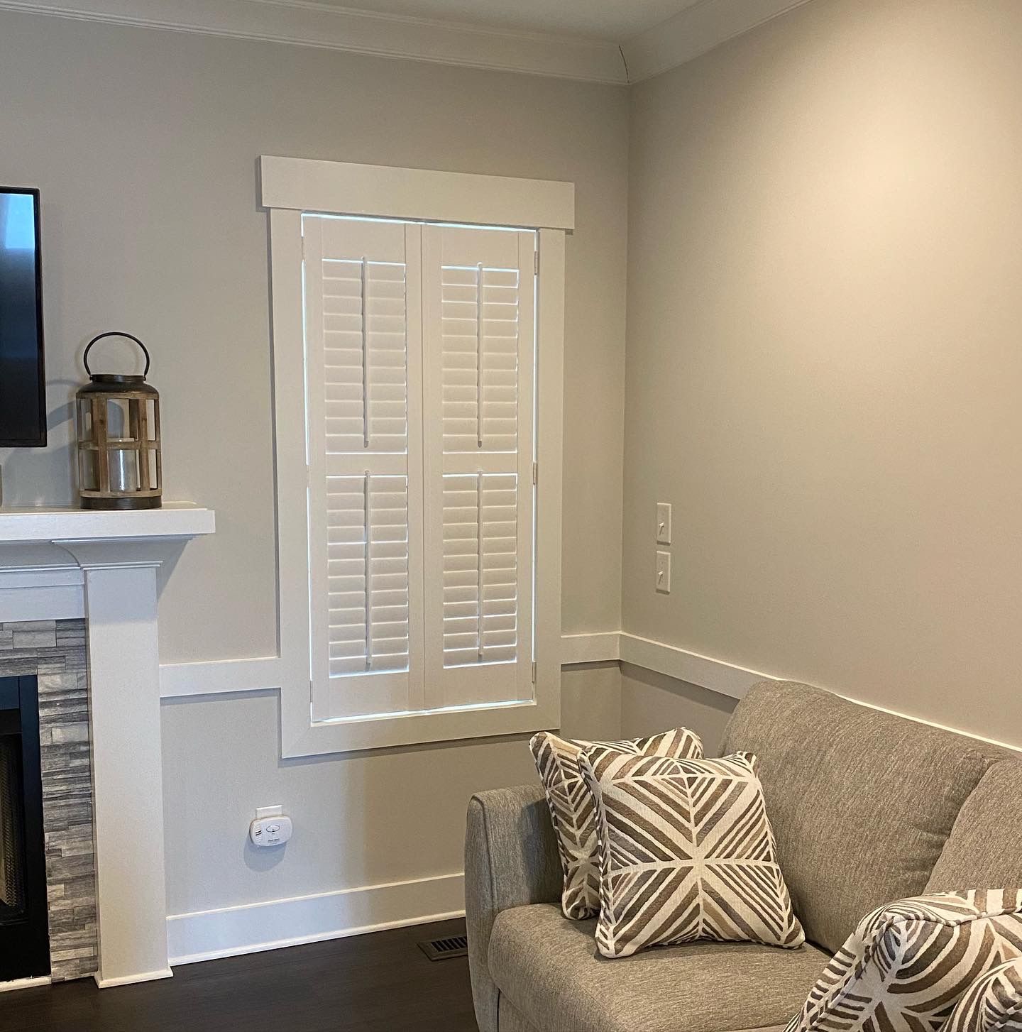 Living room with a fireplace, window with shutters, and a gray sofa with patterned pillows.
