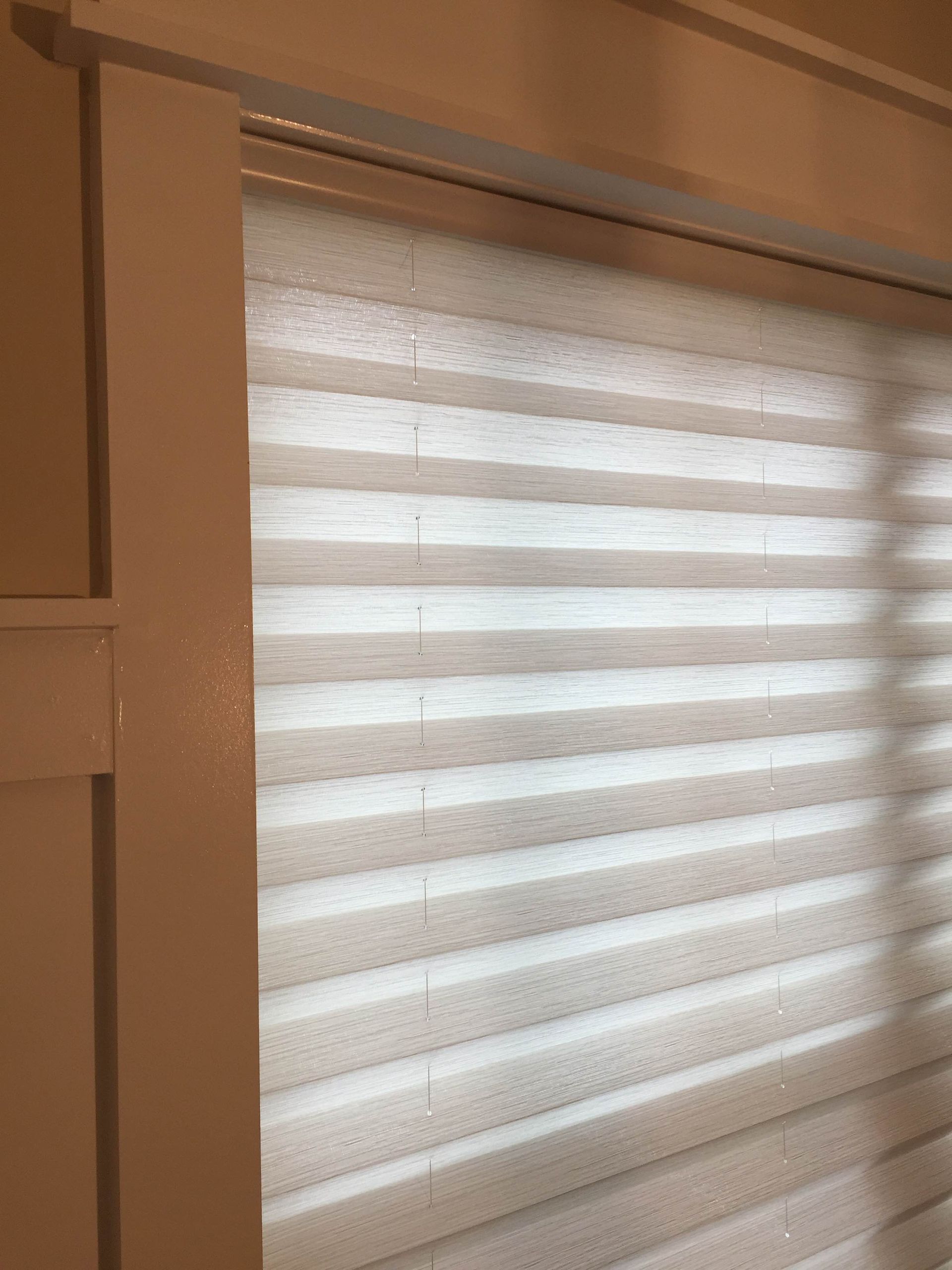 Cream-colored pleated window blinds in a white frame, partially covering a window.