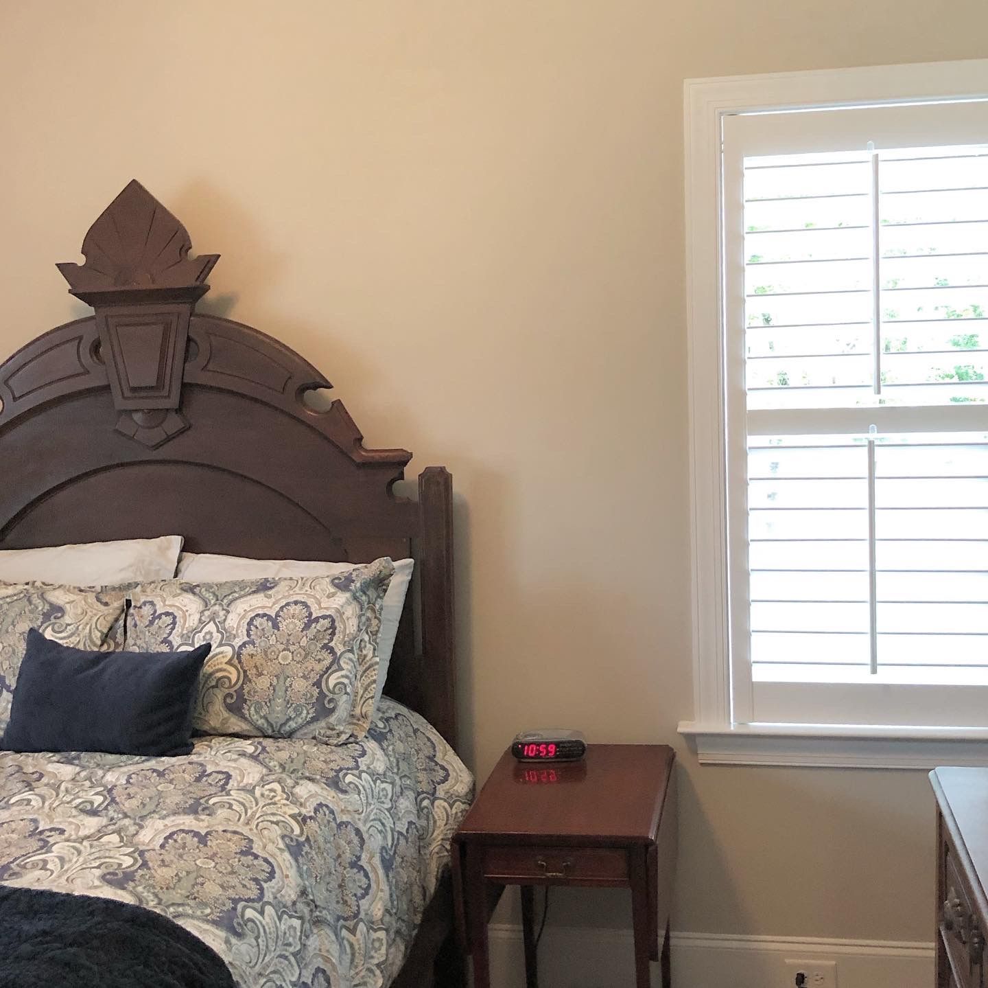 Bedroom with wooden bed and nightstand, patterned bedding, white window shutters.