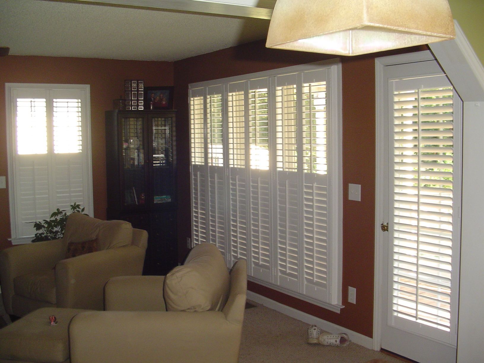 Living room with white shutters, tan armchairs, and dark brown wall.