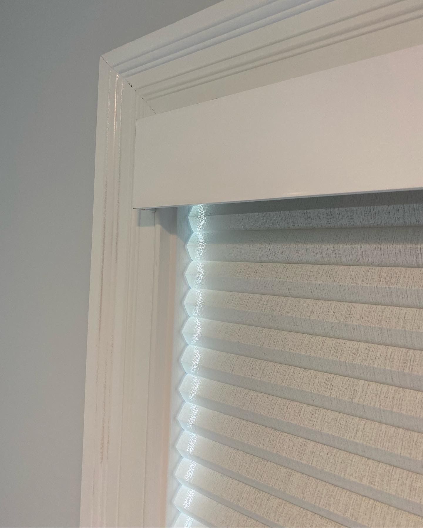 White window frame with pleated blinds partially covering the window.