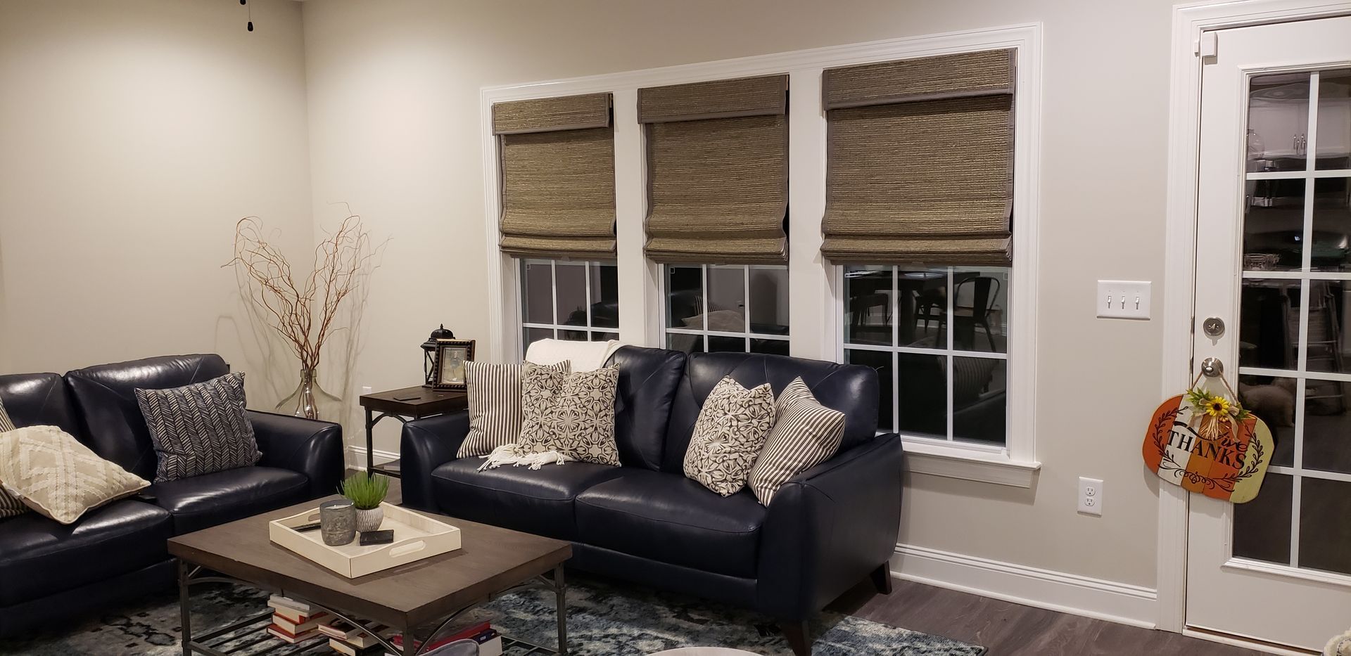 Living room with blue sofas, windows with shades, and a door with a wreath.
