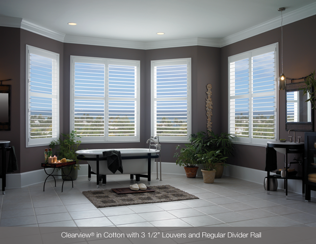 Bathroom with white shutters, a bathtub, plants, and brown walls and trim.
