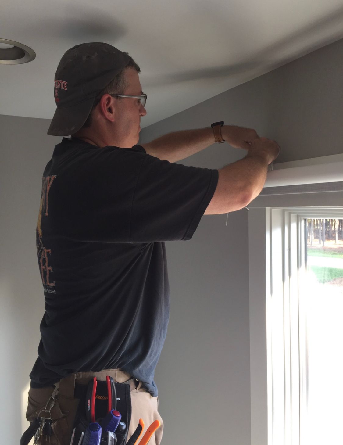 Person on a stepladder installing blinds on a window frame, indoors.