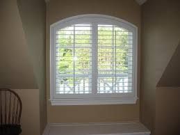 White shuttered window in an alcove with a curved top. Beige walls and a white sill.