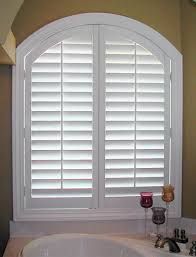 White arched window shutters in a bathroom, over a white bathtub.