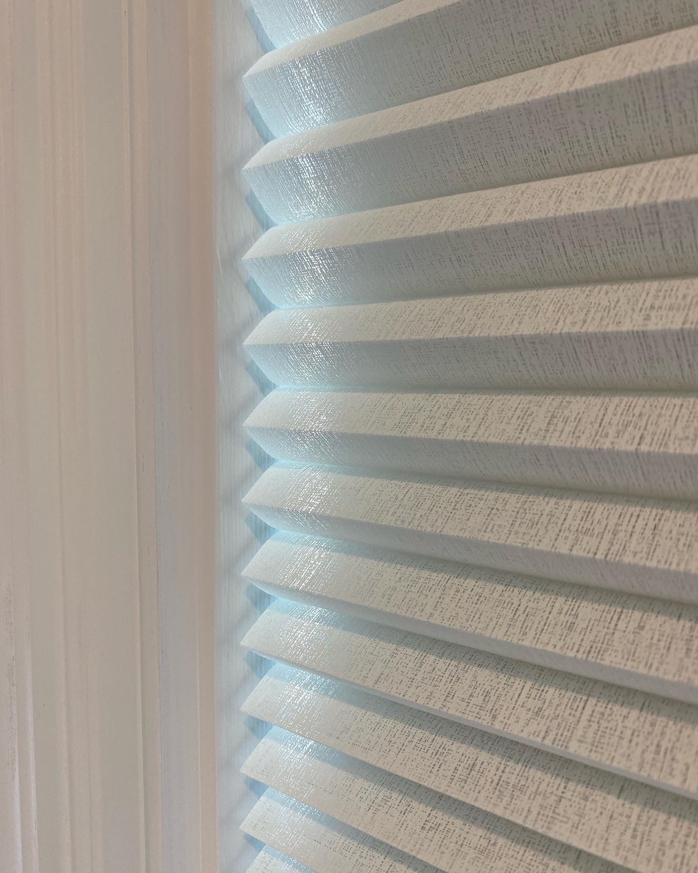 Light blue, pleated window blinds next to a sheer white curtain.