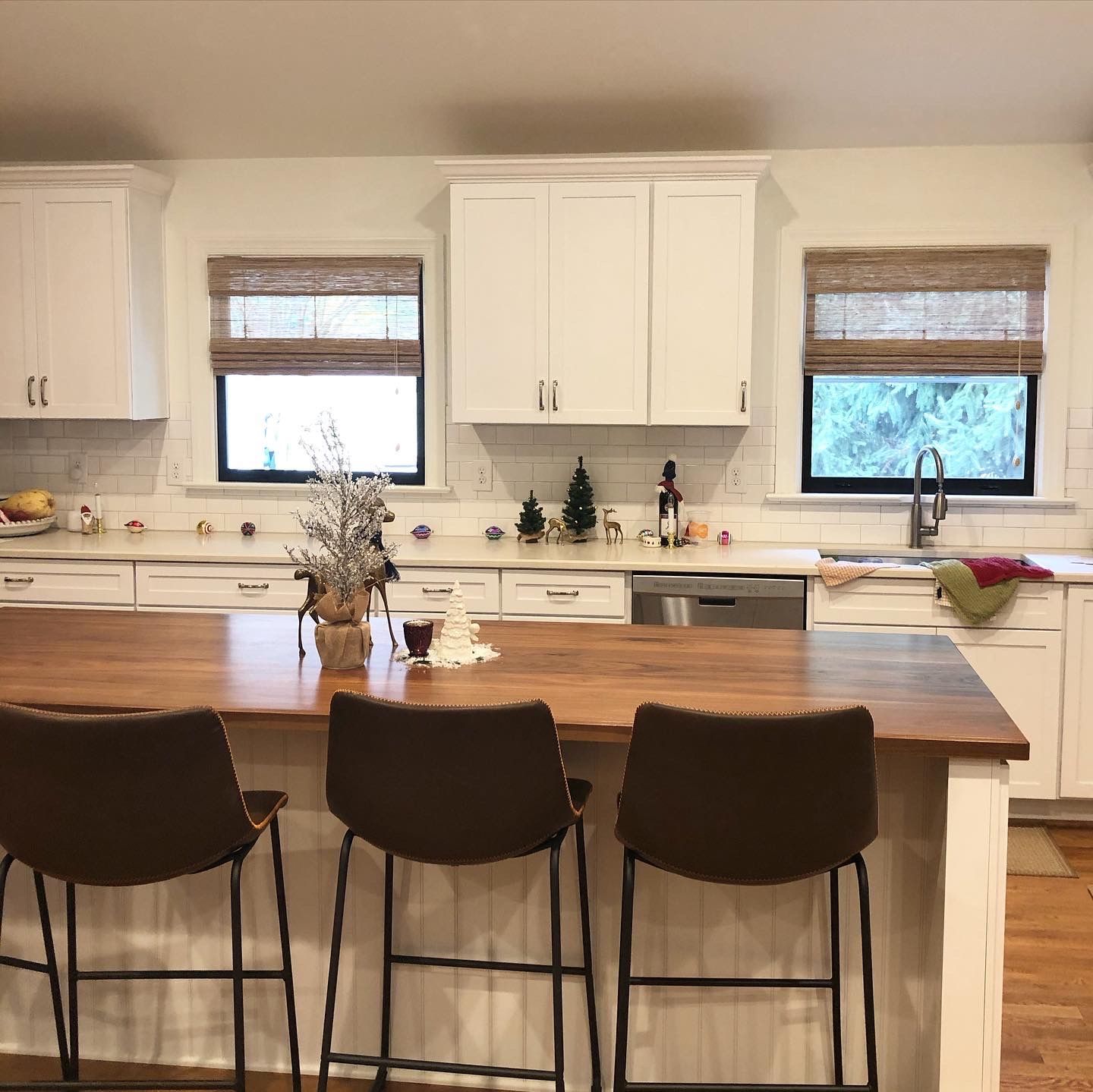 Kitchen with white cabinets, wood island, and brown bar stools. Two windows with shades.